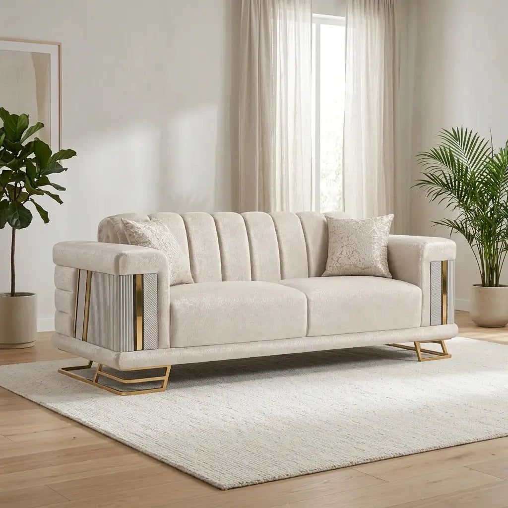 A cream-colored upholstered loveseat sofa with vertical channel tufting, gold metal side accents, and gold geometric legs