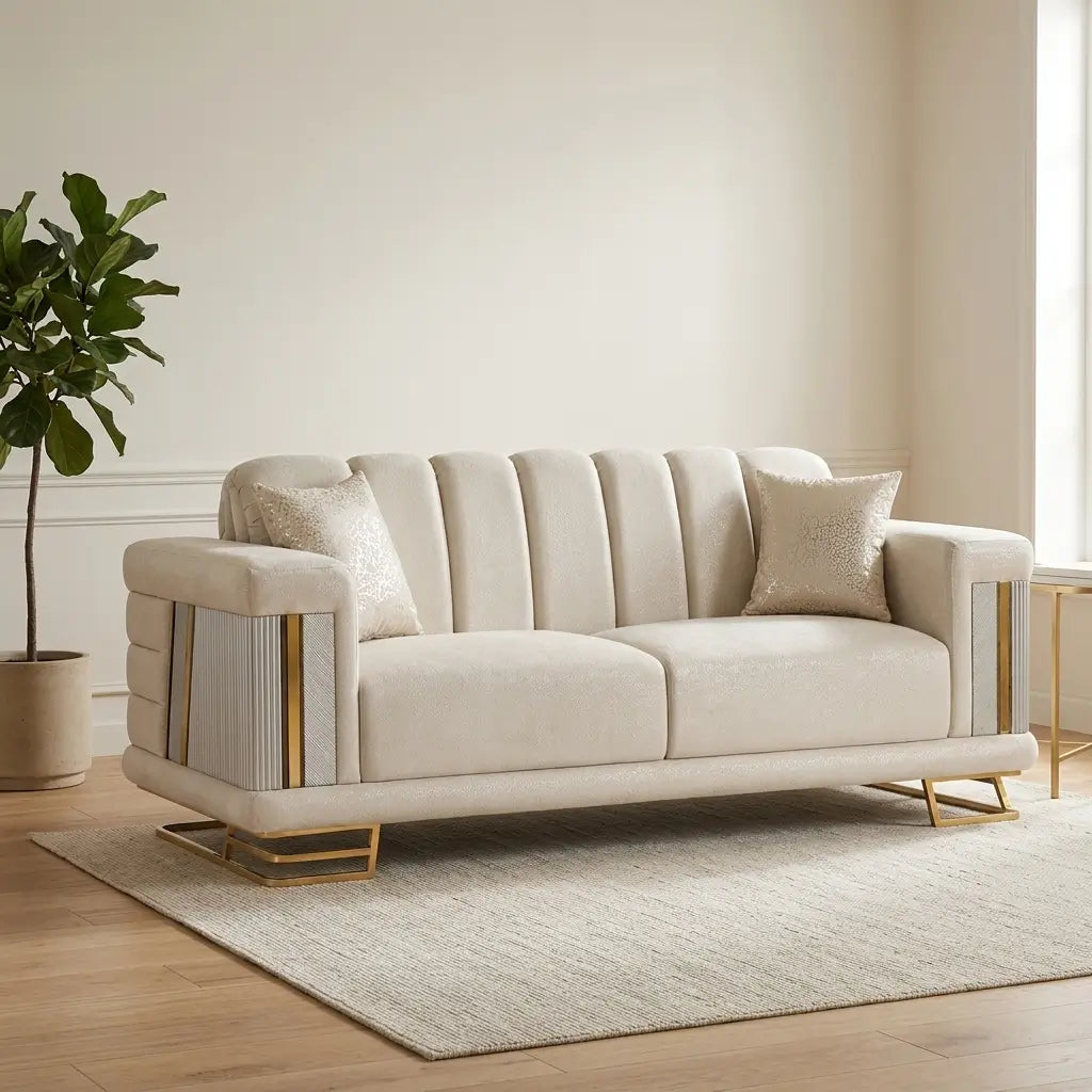 A cream-colored upholstered loveseat with vertical channel tufting on the back, fluted side panels, and gold metal legs