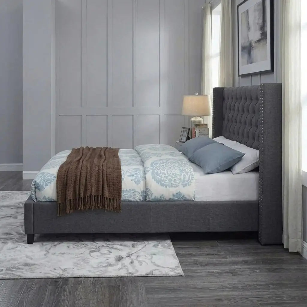 Dramatic high velvet headboard with deep button tufting and nailhead side wings above an upholstered bed frame with chrome legs